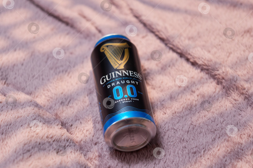 Скачать Тюмень, Россия - 11 декабря 2025 года: Банка безалкогольного пива guinness стоит на мягкой поверхности, демонстрируя выбор для тех, кто предпочитает фотосток Ozero
