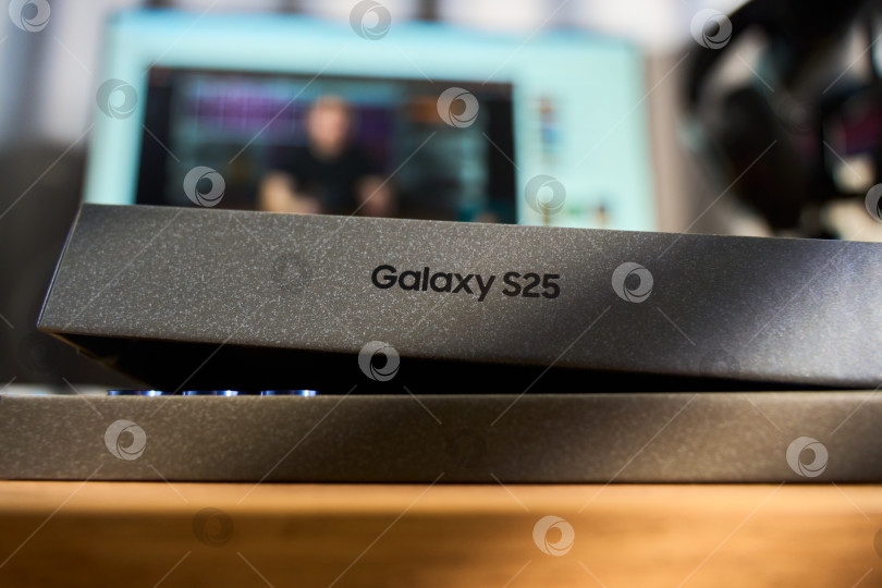 Скачать Тюмень, Россия - 3 декабря 2025 года: Новый смартфон samsung s25 стоит рядом со своей коробкой на деревянной поверхности, на которой четко видны основные детали фотосток Ozero