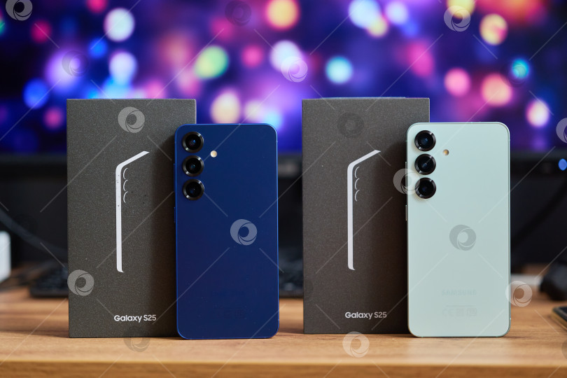 Скачать Тюмень, Россия - 11 декабря 2025 года: Два устройства Samsung S25 стоят бок о бок на деревянном столе со своими коробками фотосток Ozero
