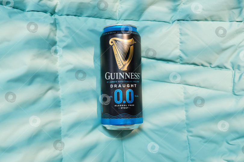 Скачать Тюмень, Россия - 11 декабря 2025 г.: Банка безалкогольного пива guinness стоит на синем покрывале. Банка оформлена в темном стиле и содержит информацию фотосток Ozero