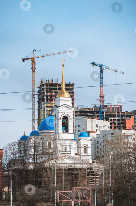 Скачать Екатеринбург, Россия, 03 апреля 2026 года. Кафедральный собор Успения Пресвятой Богородицы. На фоне городского пейзажа традиционная церковь соседствует с возвышающимися жилыми башнями и кранами фотосток Ozero