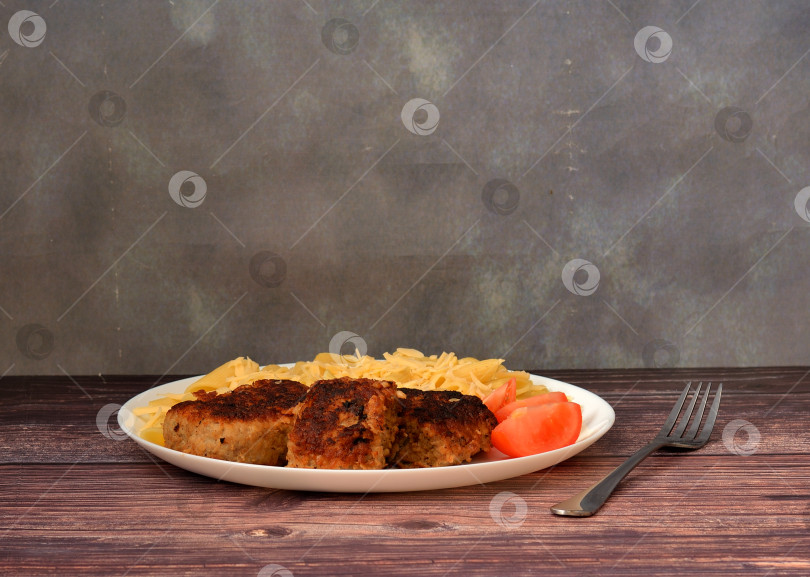 Скачать Жареные мясные котлеты, кусочки помидоров и макароны с сыром в керамической тарелке на деревянном столе. фотосток Ozero