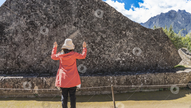 Скачать Женщина в красном пальто и шляпе стоит у огромного древнего ритуального камня. фотосток Ozero