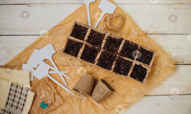 Скачать Вид сверху на семена и ячейки с почвой на деревянном фоне. Выращивание рассады в торфяных стаканчиках. Концепция весеннего озеленения дома. фотосток Ozero