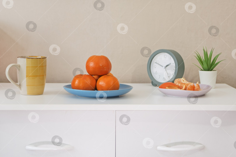 Скачать Минималистичный натюрморт с мандаринами, кофейной кружкой и будильником на белом комоде. Смотрите прямо перед собой. фотосток Ozero