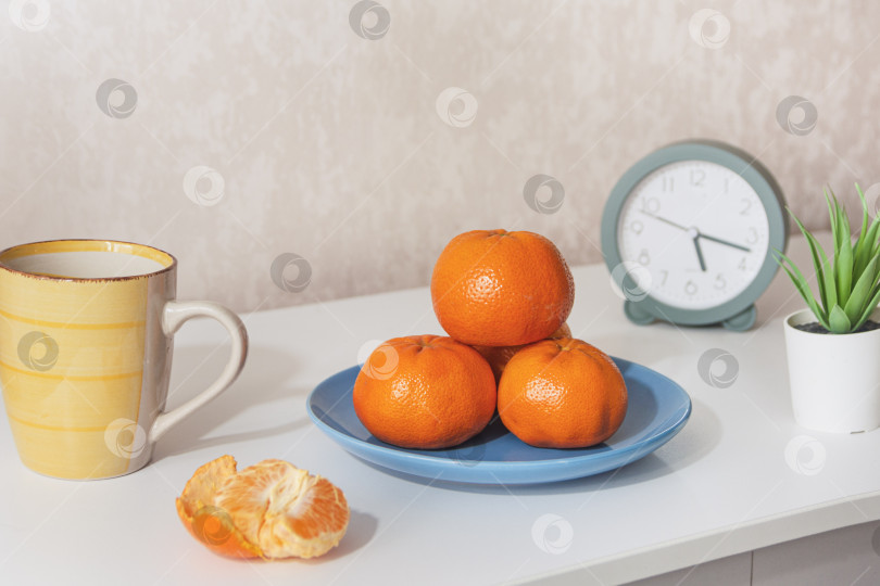 Скачать Минималистский натюрморт с мандаринами, кофейной кружкой и будильником на белом комоде фотосток Ozero