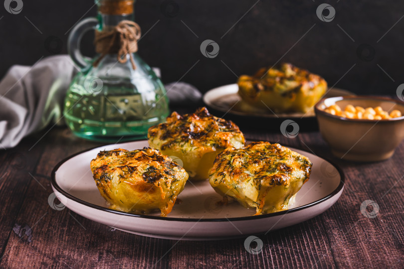 Скачать Половинки картофеля, запеченные с сыром, чесноком и зеленью на тарелке, подаются на стол фотосток Ozero