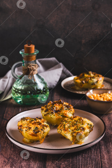 Скачать Половинки картофеля, запеченные с сыром, чесноком и зеленью на тарелке, на столе, вид сверху фотосток Ozero