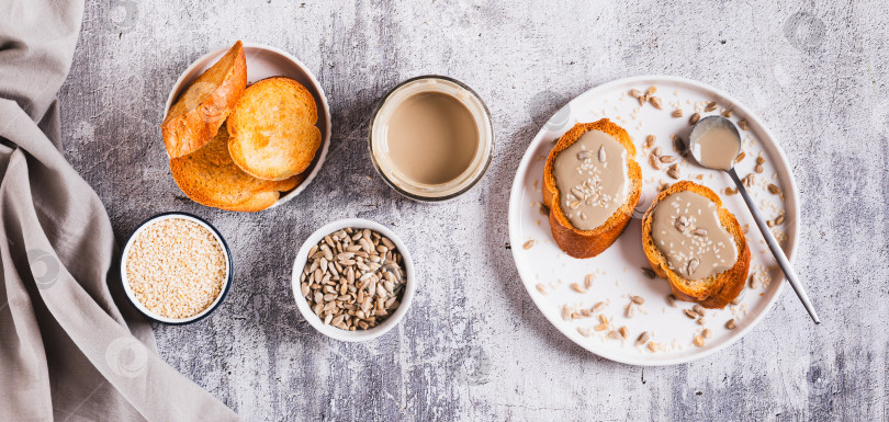 Скачать Тосты с кунжутом и подсолнечной тахини на тарелке на столешнице посмотреть веб-баннер фотосток Ozero