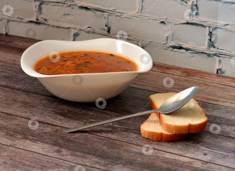 Скачать Харчо, грузинский суп со специями в глубокой тарелке, столовая ложка и два кусочка пшеничного хлеба на деревянном столе. фотосток Ozero