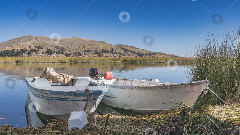 Скачать Две старые моторные лодки пришвартованы у берега плавучего острова Урос. фотосток Ozero