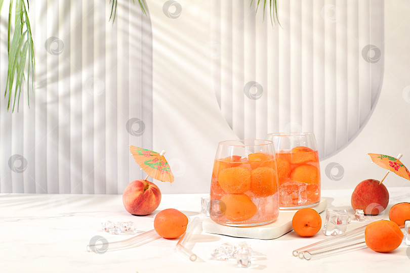 Скачать Персиковый чай со льдом или коктейль с мятой и абрикосами, рецепт освежающего летнего напитка. Два бокала с персиковым лимонадом на легком столе, концепция детокс-диеты и похудения, меню ресторана, фотосток Ozero