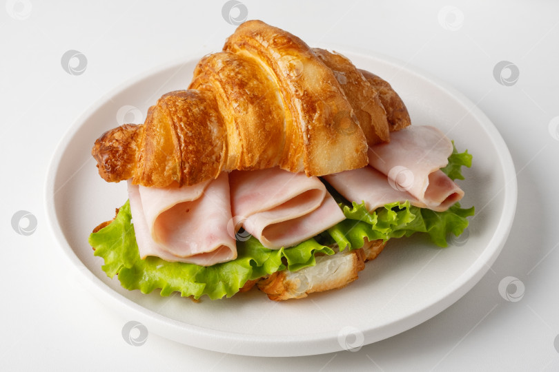 Скачать Круассан с ветчиной и листьями салата подается на белой тарелке фотосток Ozero
