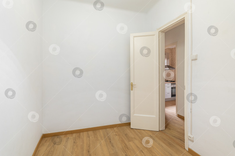 Скачать Пустая белая комната с входной дверью и видом на уютную кухню с деревянным ламинатом в новой квартире. Концепция подготовки к меблировке и новоселью. Копировальное пространство фотосток Ozero