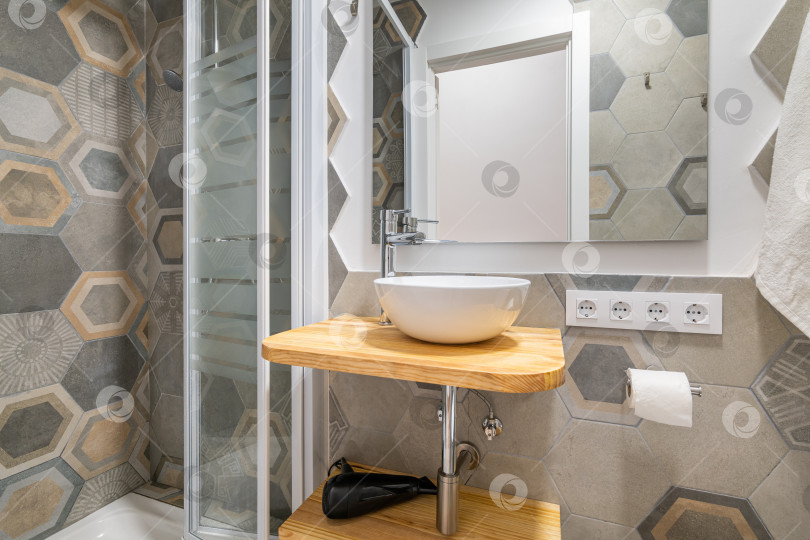 Скачать Серая плитка с многоугольным рисунком в ванной комнате с застекленной душевой кабиной и раковиной. Концепция стильной дизайнерской ванной комнаты в отеле или частном доме. Современный интерьер фотосток Ozero