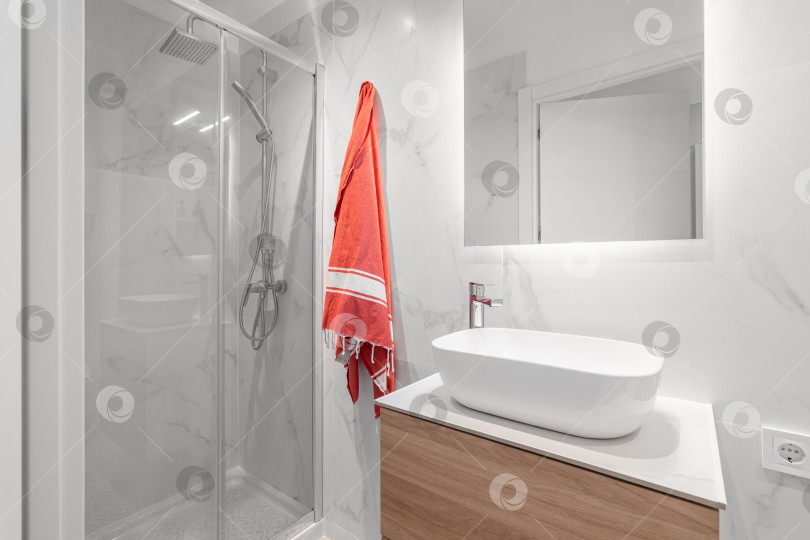 Скачать Белая компактная ванная комната со стильным ремонтом, раковиной с зеркалом и застекленной душевой кабиной. Концепция ванной комнаты в уютной квартире или загородном доме. Копировальное пространство фотосток Ozero