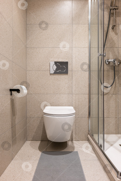 Скачать Прямой снимок небольшой ванной комнаты с белым настенным унитазом и стеклянной душевой кабиной, облицованной стильной бежевой плиткой. Концепция стильного, но простого и лаконичного дизайна в ванной комнате фотосток Ozero