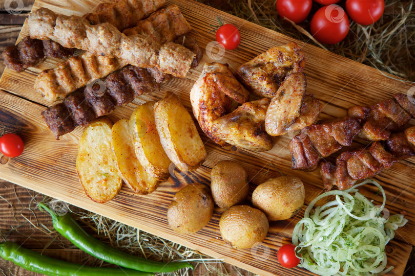 Скачать Мясные закуски, овощи и грибы, запеченные на гриле, лежат на деревянной разделочной доске. фотосток Ozero