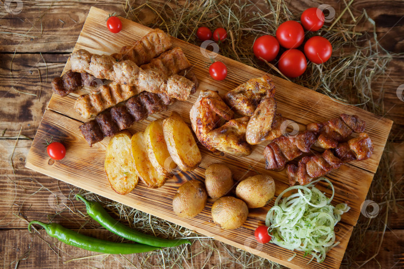 Скачать Мясные закуски, овощи и грибы, запеченные на гриле, лежат на деревянной разделочной доске. фотосток Ozero