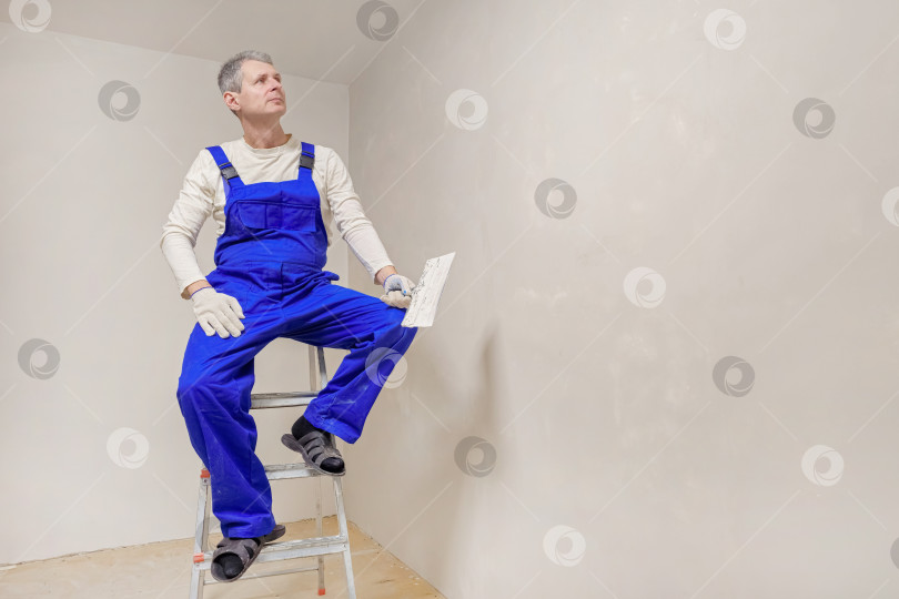 Скачать Мужчина в синем комбинезоне сидит на лестнице фотосток Ozero