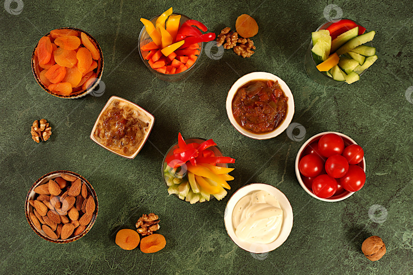 Скачать Концепция восточной кухни и полезных закусок, кухня здорового питания на фоне чаши с хумусом и палочками из сырых овощей, орехами и курагой. Блюдо с хумусом и закусками, традиционными веганскими закусками фотосток Ozero