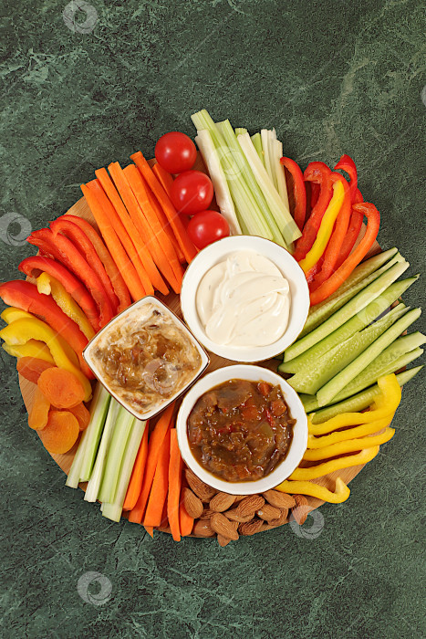 Скачать Кухня здорового питания на фоне миски с хумусом и палочками из сырых овощей, орехами и курагой. Блюдо с хумусом и закусками, ближневосточное блюдо, традиционные веганские закуски., фотосток Ozero