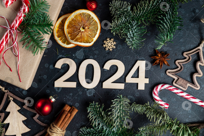 Скачать На столе лежит подарок, окруженный ветками рождественской елки, деревянными игрушками, специями и цифрами 2024 фотосток Ozero
