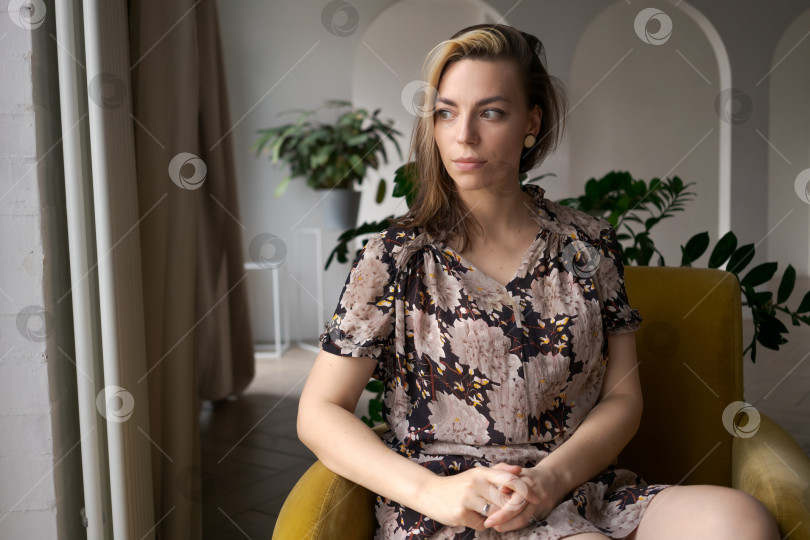 Скачать Женщина в летнем платье в цветочек Задумчиво смотрит в сторону в ярком Биофильном жилом пространстве фотосток Ozero