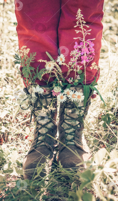 Скачать Женские ноги в тяжелых ботинках с полевыми цветами, воткнутыми в шнурки. Платье развевается на ветру фотосток Ozero