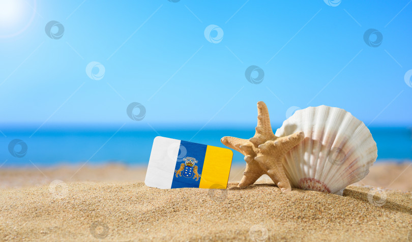 Скачать Тропический пляж с ракушками и флагом Канарских островов. Концепция райского отдыха на пляжах Канарских островов. фотосток Ozero