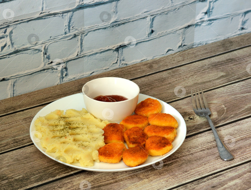 Скачать Тарелка с легким обедом, жареные куриные наггетсы с картофельным пюре и кетчупом на деревянном столе. фотосток Ozero