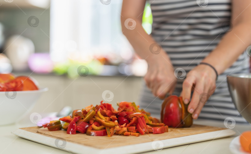 Скачать Крупный план женщины, режущей болгарский перец кухонным ножом на ярко освещенной кухне. фотосток Ozero