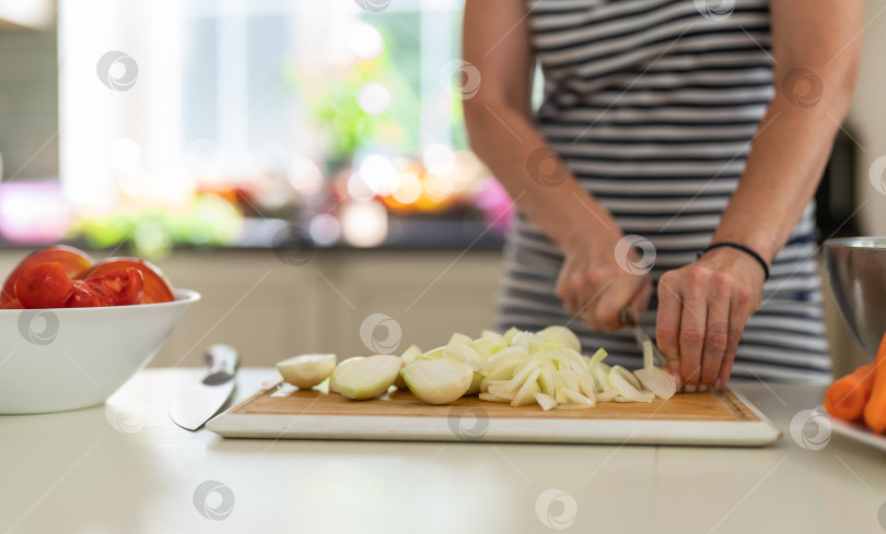Скачать Крупный план женщины, режущей лук кухонным ножом на ярко освещенной кухне. фотосток Ozero