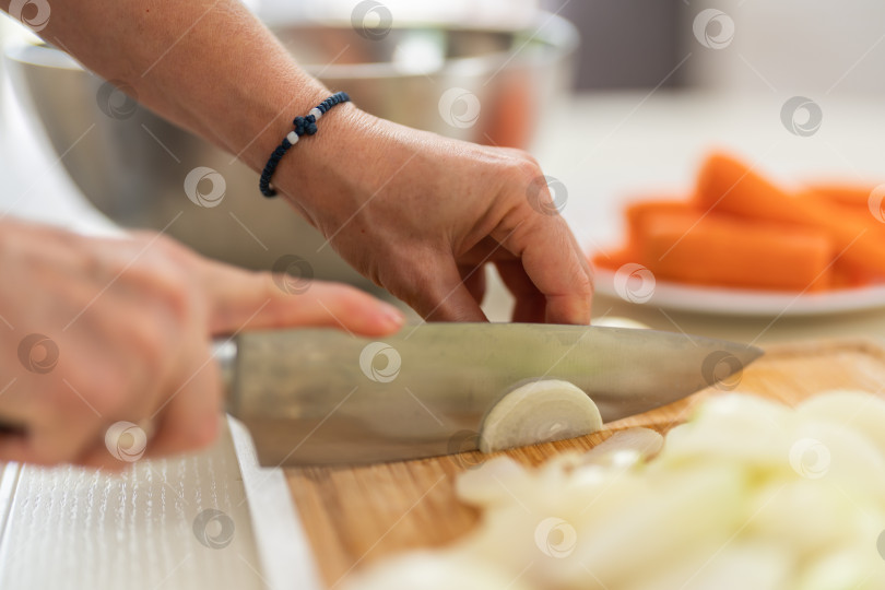 Скачать Крупный план женщины, режущей лук кухонным ножом на ярко освещенной кухне. фотосток Ozero