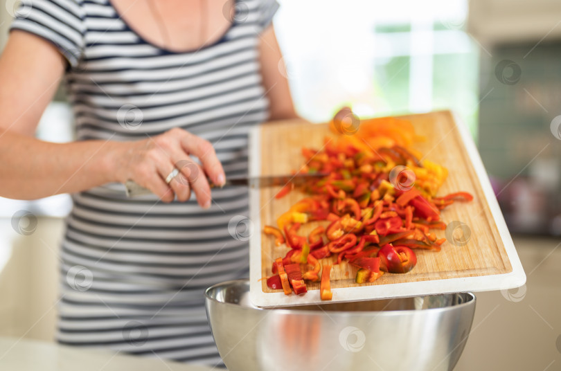 Скачать Крупный план женщины, режущей болгарский перец кухонным ножом на ярко освещенной кухне. фотосток Ozero