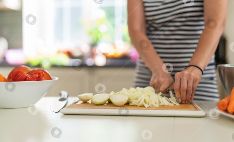 Скачать Крупный план женщины, режущей лук кухонным ножом на ярко освещенной кухне. фотосток Ozero