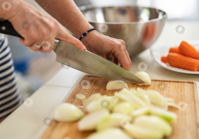 Скачать Крупный план женщины, режущей лук кухонным ножом на ярко освещенной кухне. фотосток Ozero