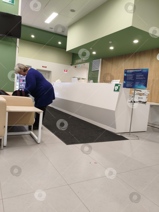 Скачать Женщина в синем свитере стоит недалеко от стойки регистрации в медицинском центре. Москва,Коммунарка, 1.03.2026г фотосток Ozero