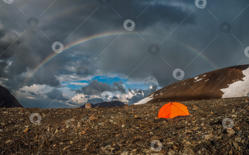 Скачать Панорама с радугой и оранжевой палаткой в горах. Атмосферный альпийский пейзаж со снежными горами и радугой в дождливую и солнечную погоду. фотосток Ozero