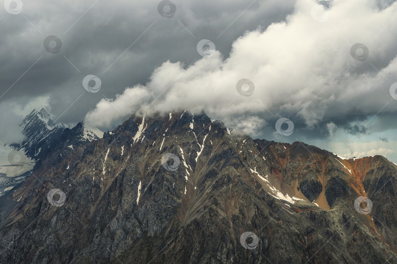 Скачать Чудесный пейзаж с большими заснеженными горными вершинами над низкими облаками. Атмосферные большие снежные горные вершины в облачном небе. фотосток Ozero