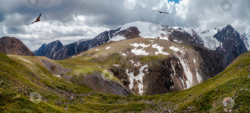 Скачать Живописный панорамный горный пейзаж с огромными скалами на фоне облачного неба. Красивая коричневая скала в солнечном свете и низких облаках. фотосток Ozero