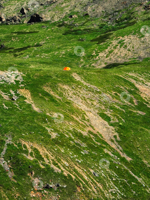 Скачать Минималистичный пейзаж зеленого горного склона с небольшой палаткой. Живописный альпийский пейзаж с палаткой на зеленом холме среди скал. Вертикальный вид. фотосток Ozero