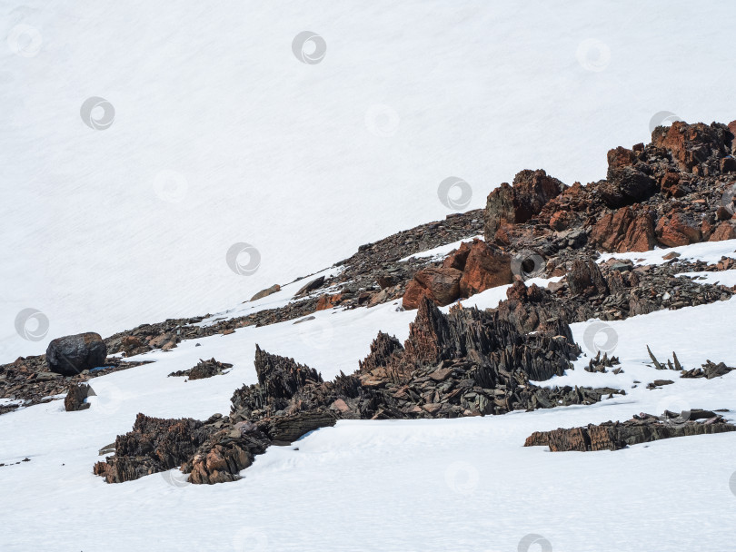 Скачать Высокогорный пейзаж с заостренными камнями необычной формы. Удивительный живописный горный пейзаж с большими потрескавшимися заостренными камнями крупным планом среди снега под голубым небом в солнечном свете. Острые камни. фотосток Ozero