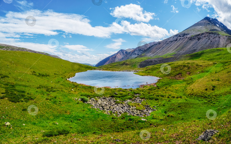 Скачать Ярко-зелено-голубой альпийский пейзаж с горным озером в высокогорной долине в солнечном свете и большой горой под голубым облачным небом. Тень облаков на зеленой горной долине. Панорамный вид. фотосток Ozero