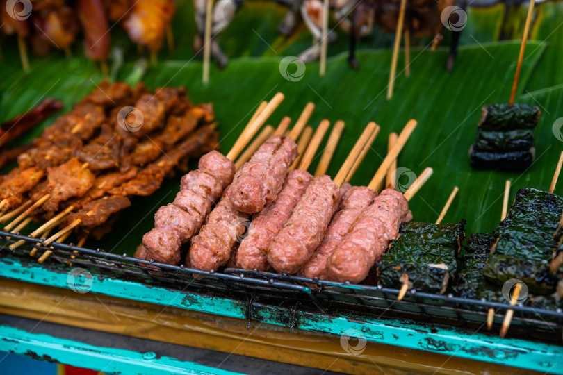 Скачать Традиционные свиные фрикадельки на гриле нэм нуонг и мясо, завернутое в листья бетеля бо ла лот, нанизанные на шпажки на открытом рынке уличной еды во Вьетнаме фотосток Ozero