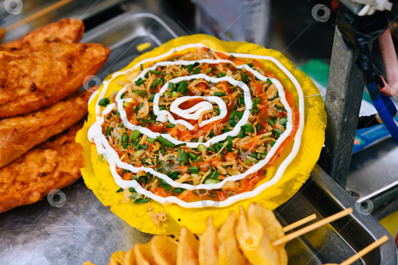 Скачать Вкуснейшую Бань Транг Нуонг, известную как вьетнамская пицца на рисовой бумаге с соусами, готовят на уличном продуктовом рынке во Вьетнаме фотосток Ozero