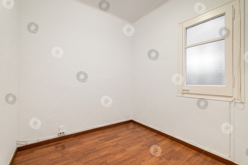 Скачать Пустая комната с ламинатным полом, недавно выкрашенными в белый цвет стенами и светлым окном с матовым стеклом. Концепция ремонта и строительства. фотосток Ozero