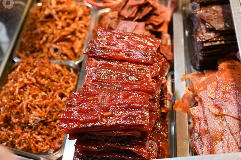 Скачать Традиционная китайская бакква, сладкое вяленое мясо из свинины и измельченная мясная нить в металлических лотках на витрине местного магазина уличной еды в Макао фотосток Ozero