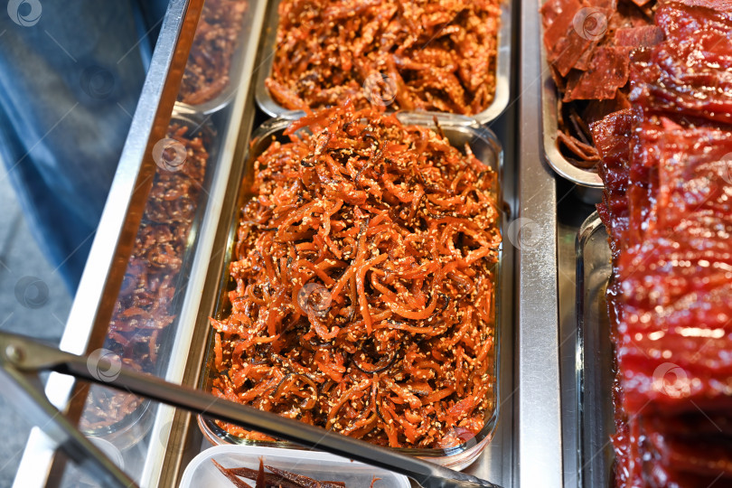 Скачать Традиционная китайская нарезанная сладкая вяленая свинина, мясная мулине с кунжутом в стеклянном лотке на витрине пекарни street food в Макао фотосток Ozero