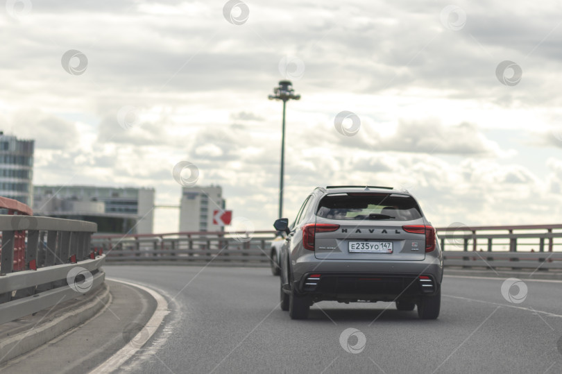 Скачать Китайский внедорожник Haval на шоссе под Санкт-Петербургом, июнь 2026 года, современный, темного цвета, быстро едет под пасмурным летним небом. фотосток Ozero